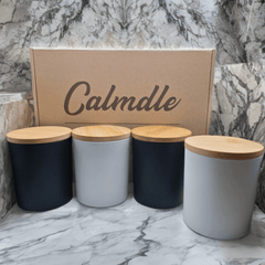 Set Complet De Bougies Parfumees Calmdle avec quatre bougies parfumees dans des contenants noirs et blancs et des couvercles en bois